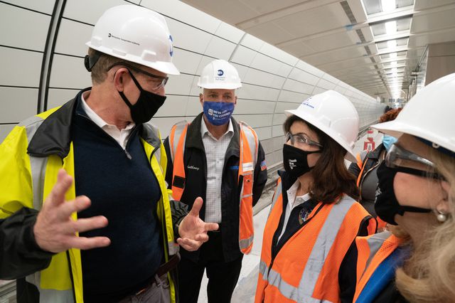 Governor Hochul, wearing a mask and a safety vest, talks to MTA officials while inspecting the East Side Access Project